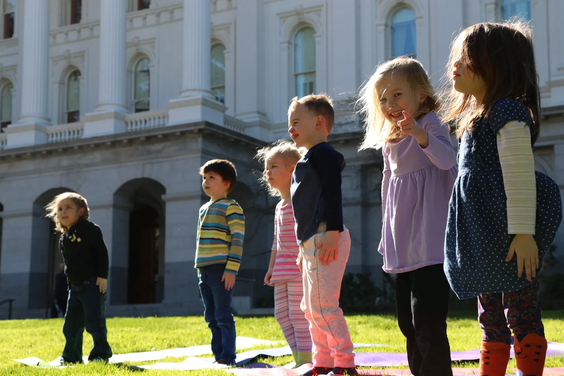 Children at Growing Mindfully lined up on the Capitol lawn, one girl smiling and pointing at the camera.